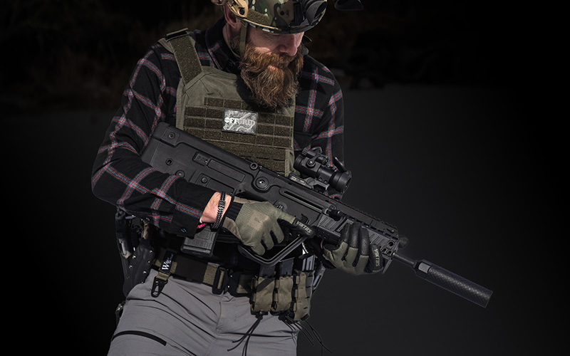 OGS-About-Us-Operator Person wearing tactical gear, gloves, and a helmet with night vision equipment holding a rifle equipped with an Off Grid Suppressors Trident TI titanium suppressor in a low-ready position.